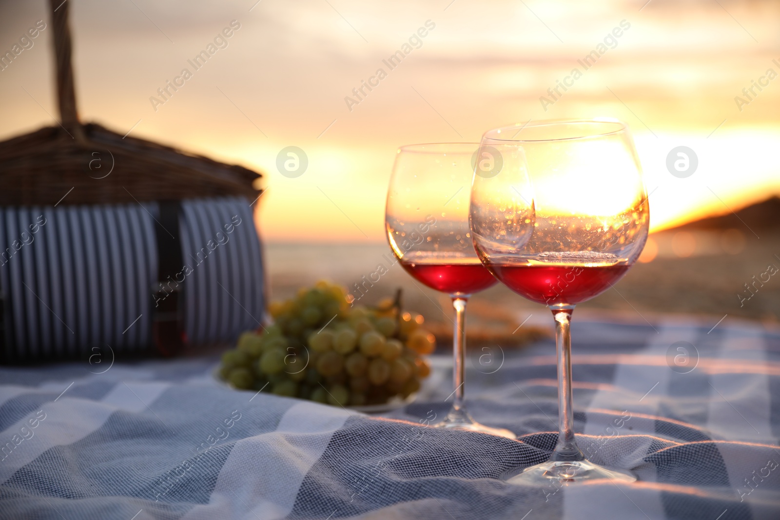 Photo of Blanket with glasses of wine and food on beach at sunset. Romantic picnic for couple