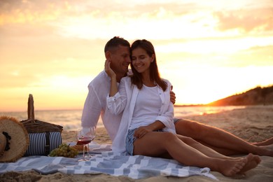 Lovely couple having romantic picnic on beach at sunset