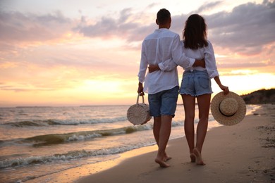 Photo of Lovely couple walking on beach at sunset, back view. Space for text