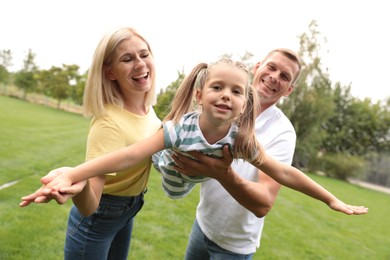 Photo of Cute little girl having fun with her parents in park on summer day