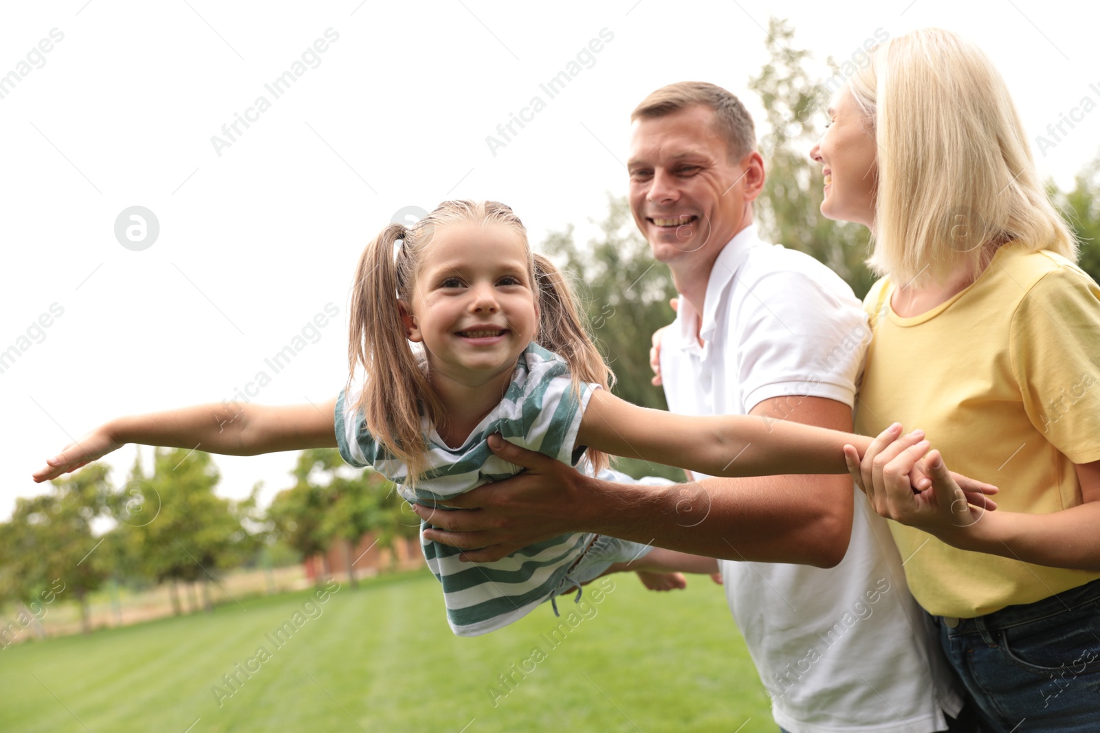 Photo of Cute little girl having fun with her parents in park on summer day