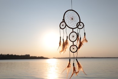 Photo of Beautiful handmade dream catcher near river at sunset. Space for text