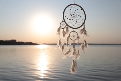 Photo of Beautiful handmade dream catcher near river at sunset. Space for text