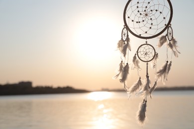 Photo of Beautiful handmade dream catcher near river at sunset. Space for text