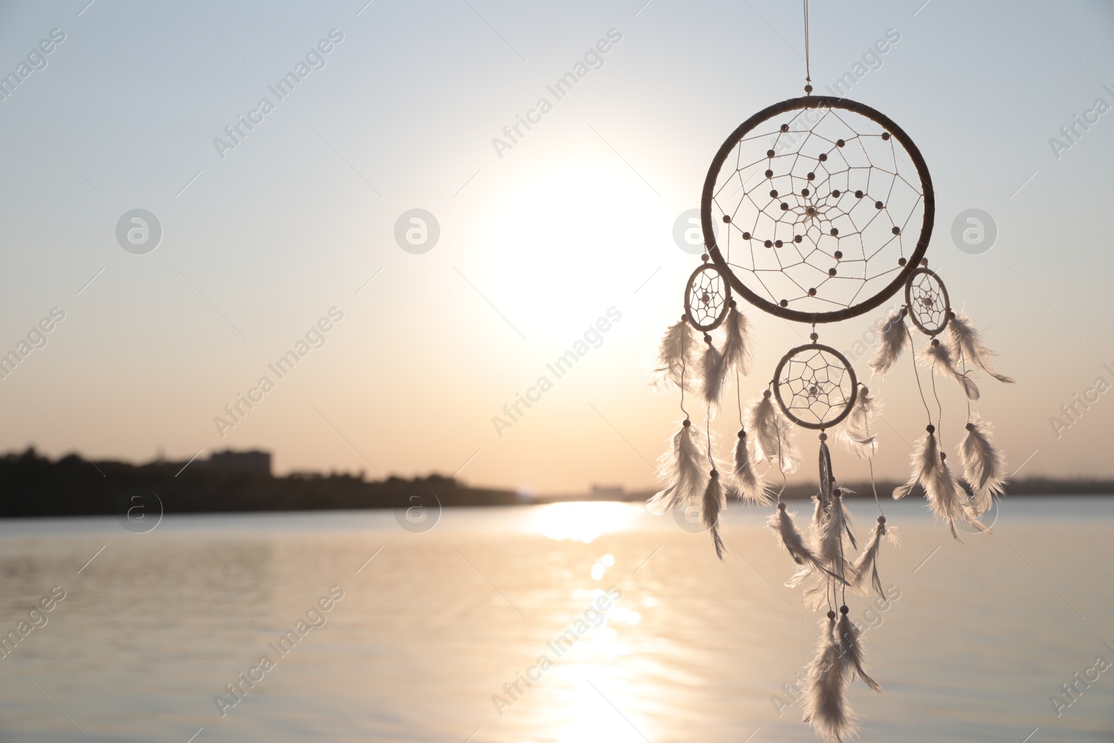 Photo of Beautiful handmade dream catcher near river at sunset. Space for text