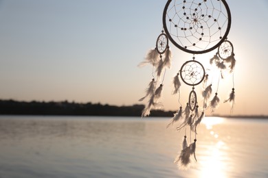 Photo of Beautiful handmade dream catcher near river at sunset. Space for text