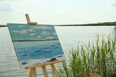 Photo of Wooden easel with unfinished painting near lake