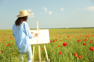 Photo of Woman painting on easel in beautiful poppy field, back view