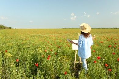 Photo of Woman painting on easel in beautiful poppy field, back view