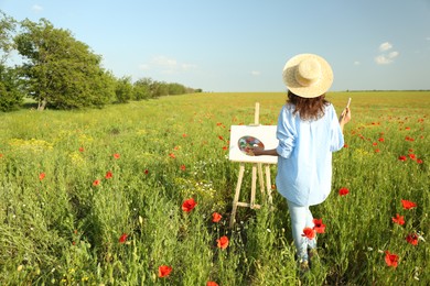 Photo of Woman painting on easel in beautiful poppy field, back view