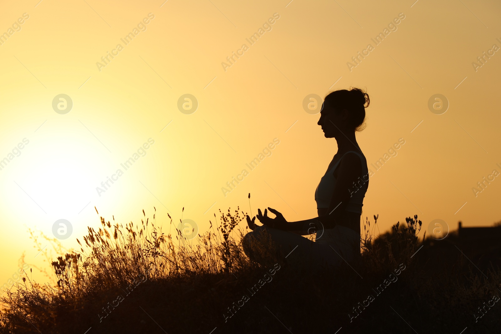 Photo of Silhouette of woman meditating outdoors at sunset. Space for text