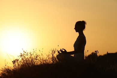 Photo of Silhouette of woman meditating outdoors at sunset. Space for text