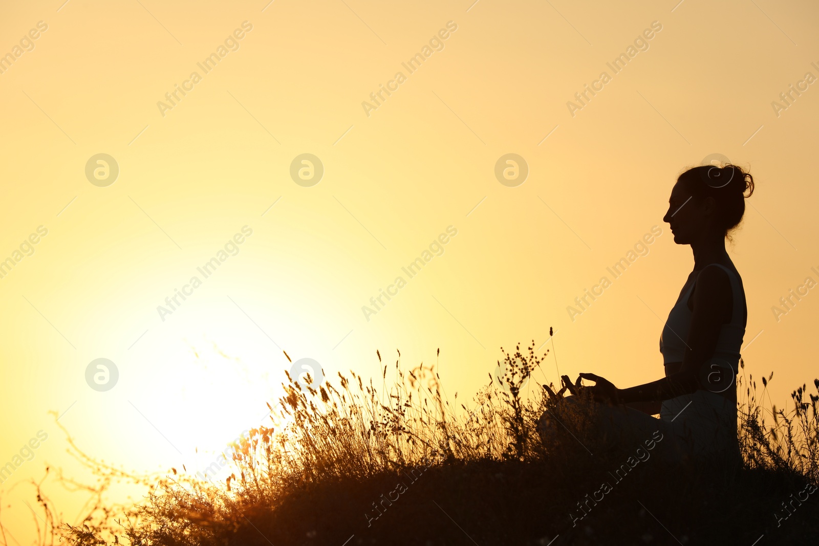 Photo of Silhouette of woman meditating outdoors at sunset. Space for text