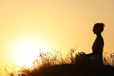 Photo of Silhouette of woman meditating outdoors at sunset. Space for text