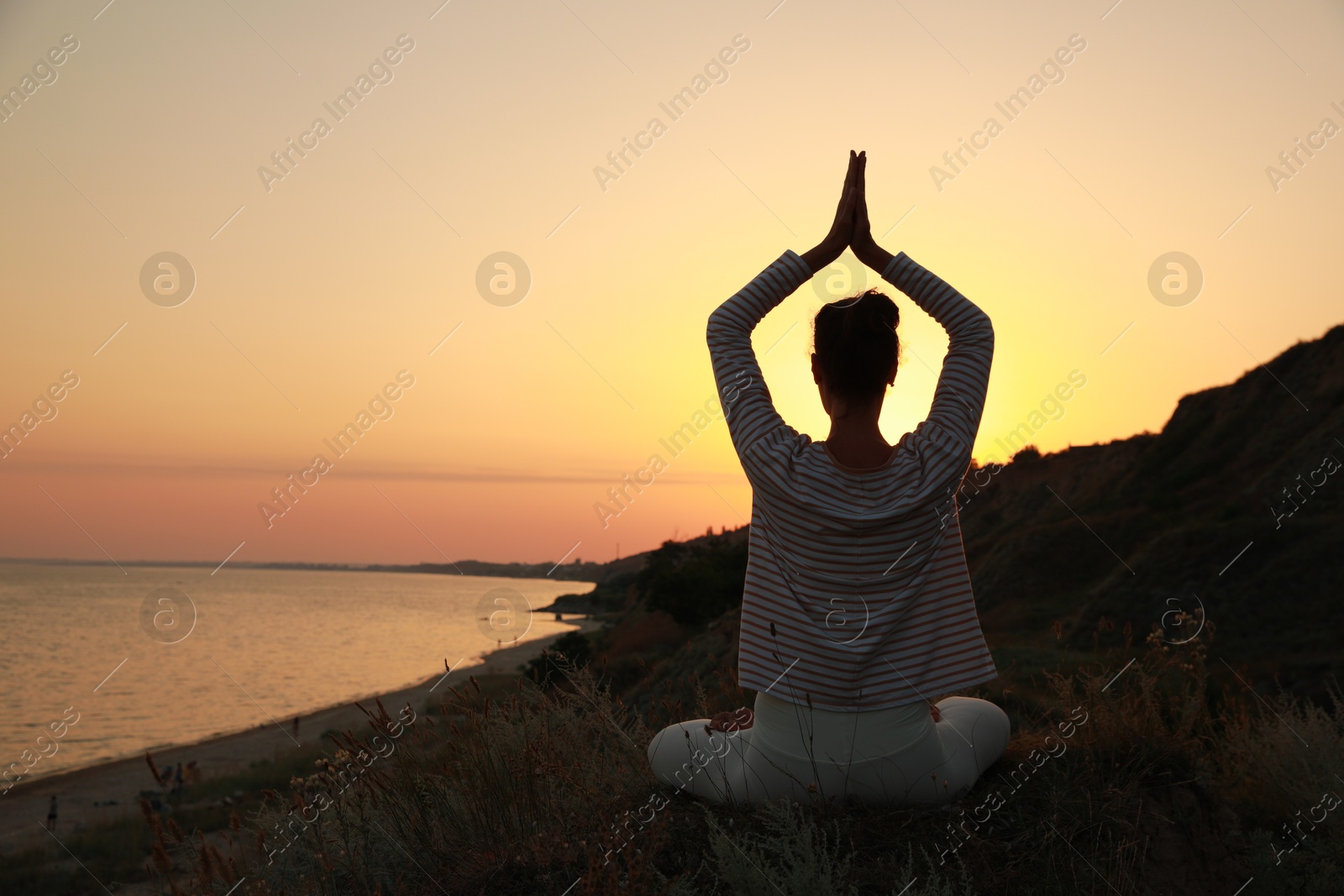 Photo of Woman meditating near sea at sunset, back view. Space for text