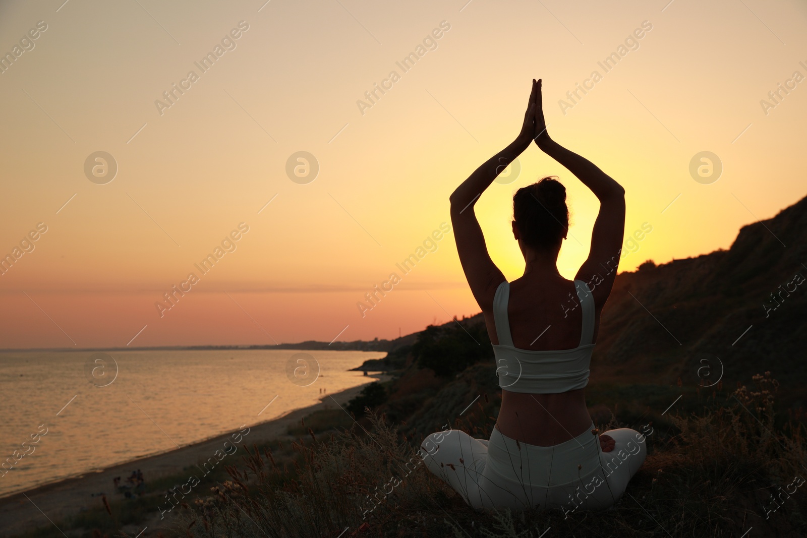 Photo of Woman meditating near sea at sunset, back view. Space for text