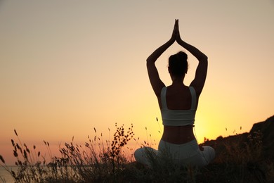 Photo of Woman meditating outdoors at sunset, back view. Space for text