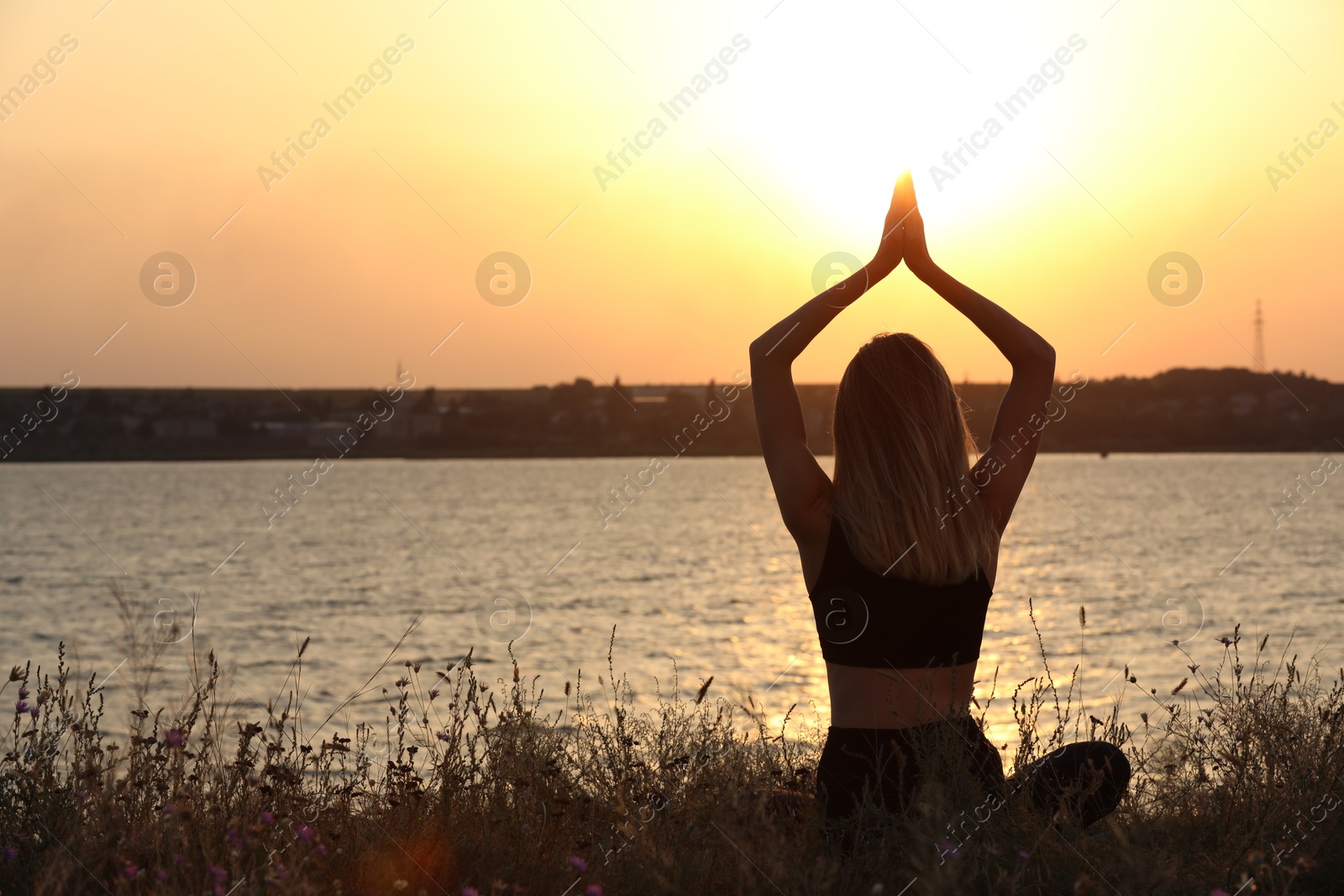 Photo of Young woman meditating near river at sunset, back view. Space for text