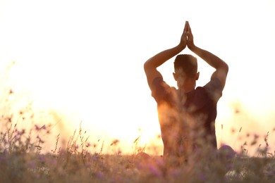 Photo of Man meditating on hill at sunset, back view. Space for text