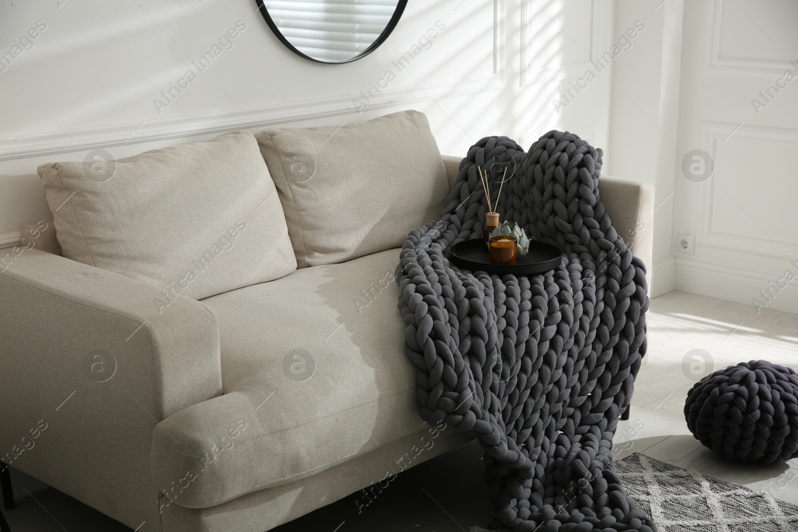 Photo of Soft chunky knit blanket and tray with decor on sofa in living room. Interior design