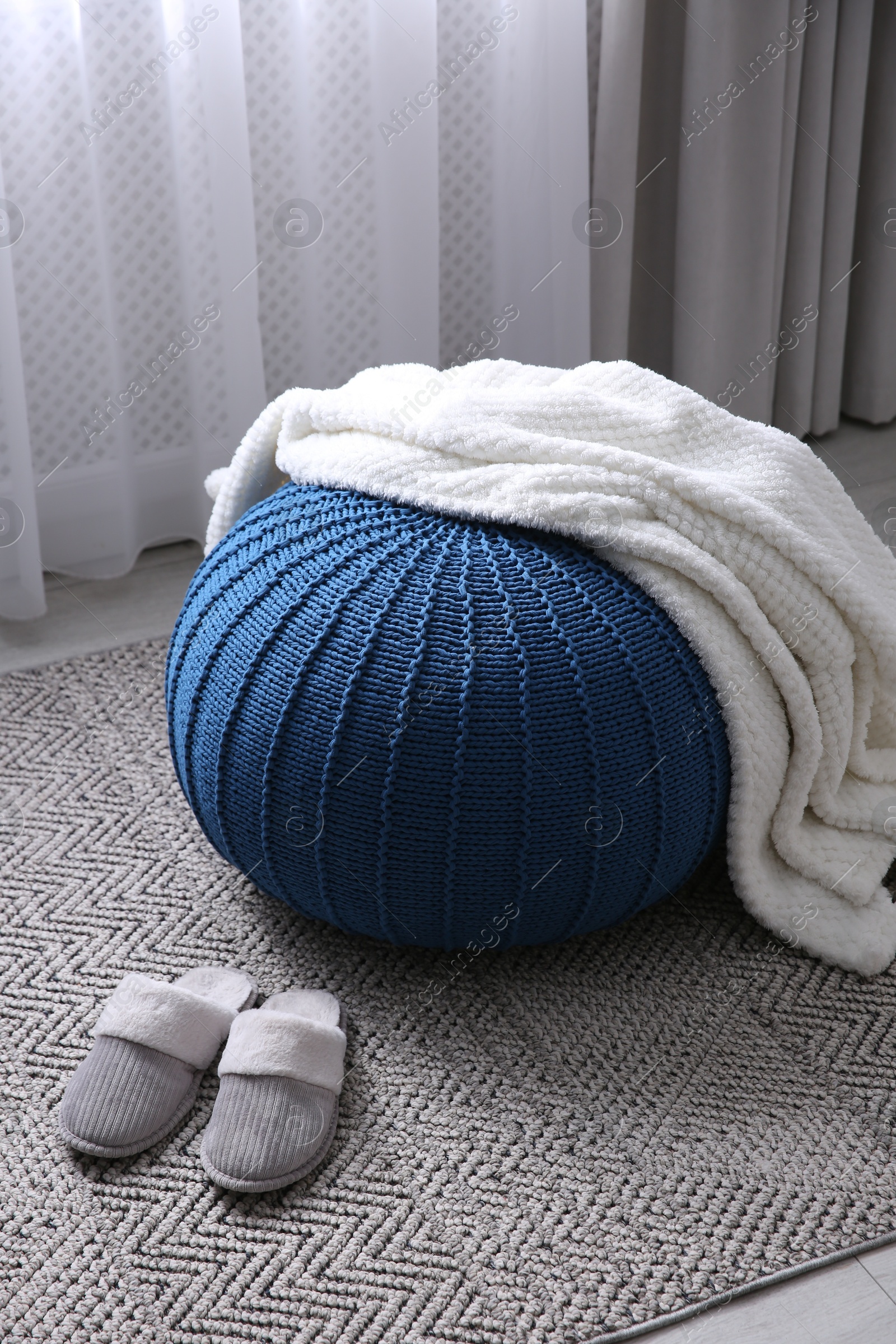 Photo of Soft blanket on blue pouf and slippers in room