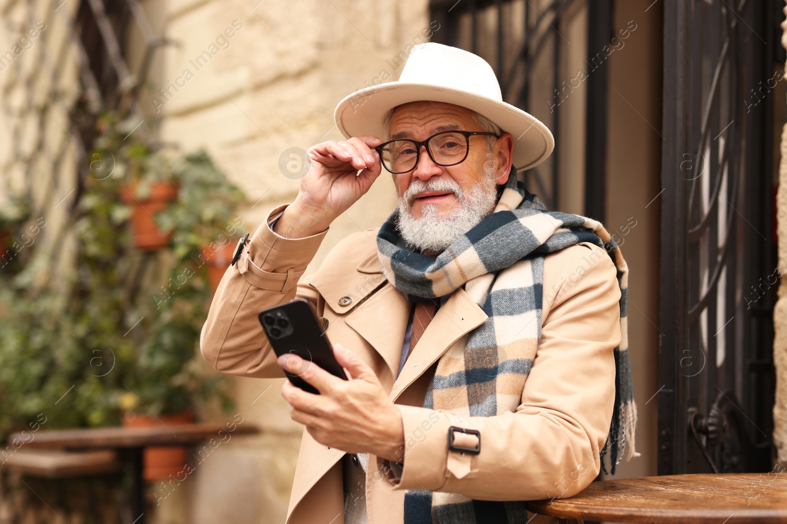 Photo of Stylish senior man with smartphone in outdoor bar