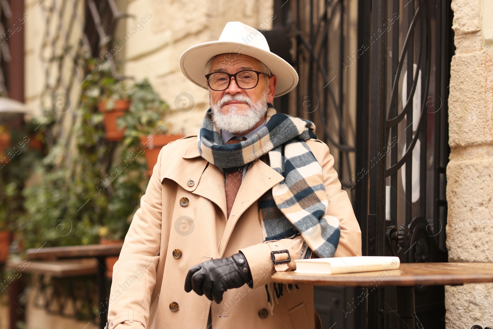 Photo of Stylish senior man with hat and scarf in outdoor bar