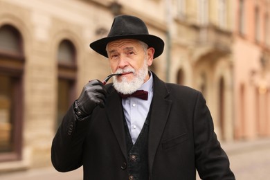 Photo of Stylish senior man with tobacco pipe on city street