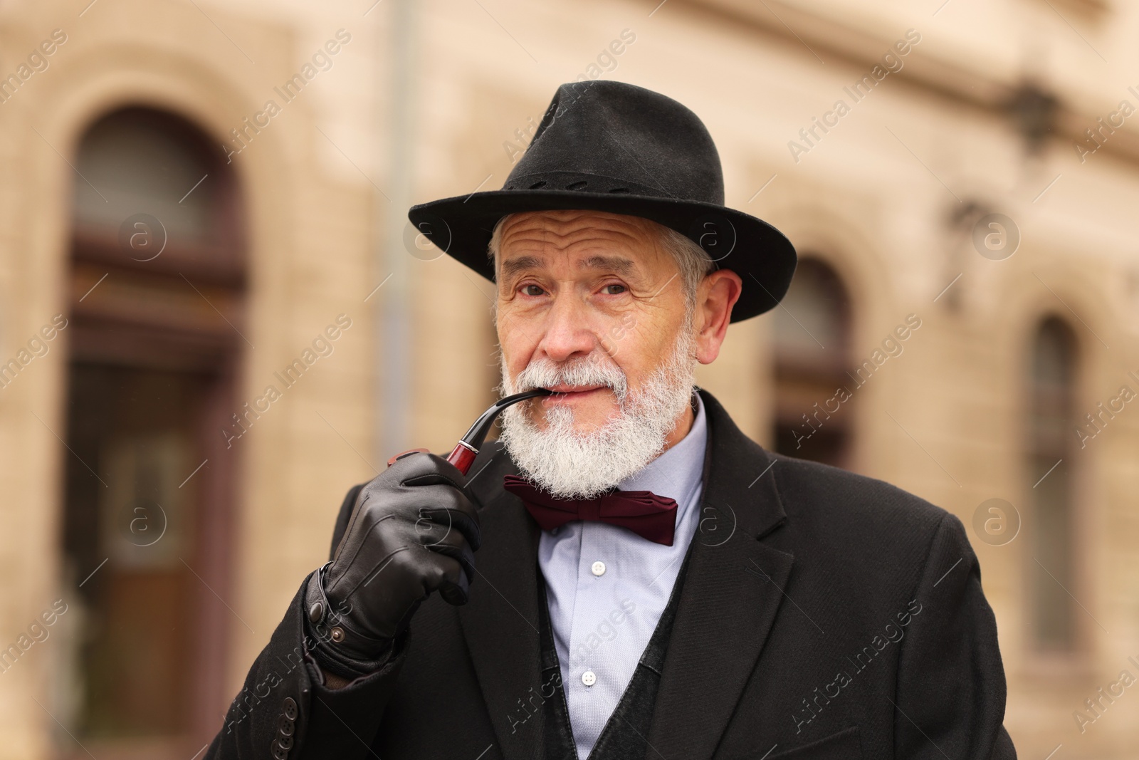 Photo of Stylish senior man with tobacco pipe on city street