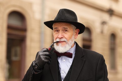 Photo of Stylish senior man with tobacco pipe on city street