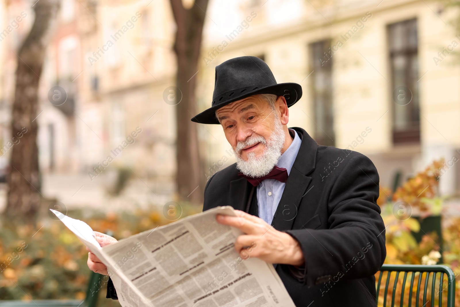 Photo of Elegant bearded man reading newspaper on bench in park