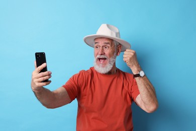 Photo of Emotional senior man with smartphone on light blue background