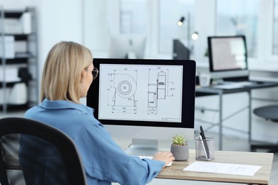 Technician making digital engineering drawing on computer at desk in office, back view