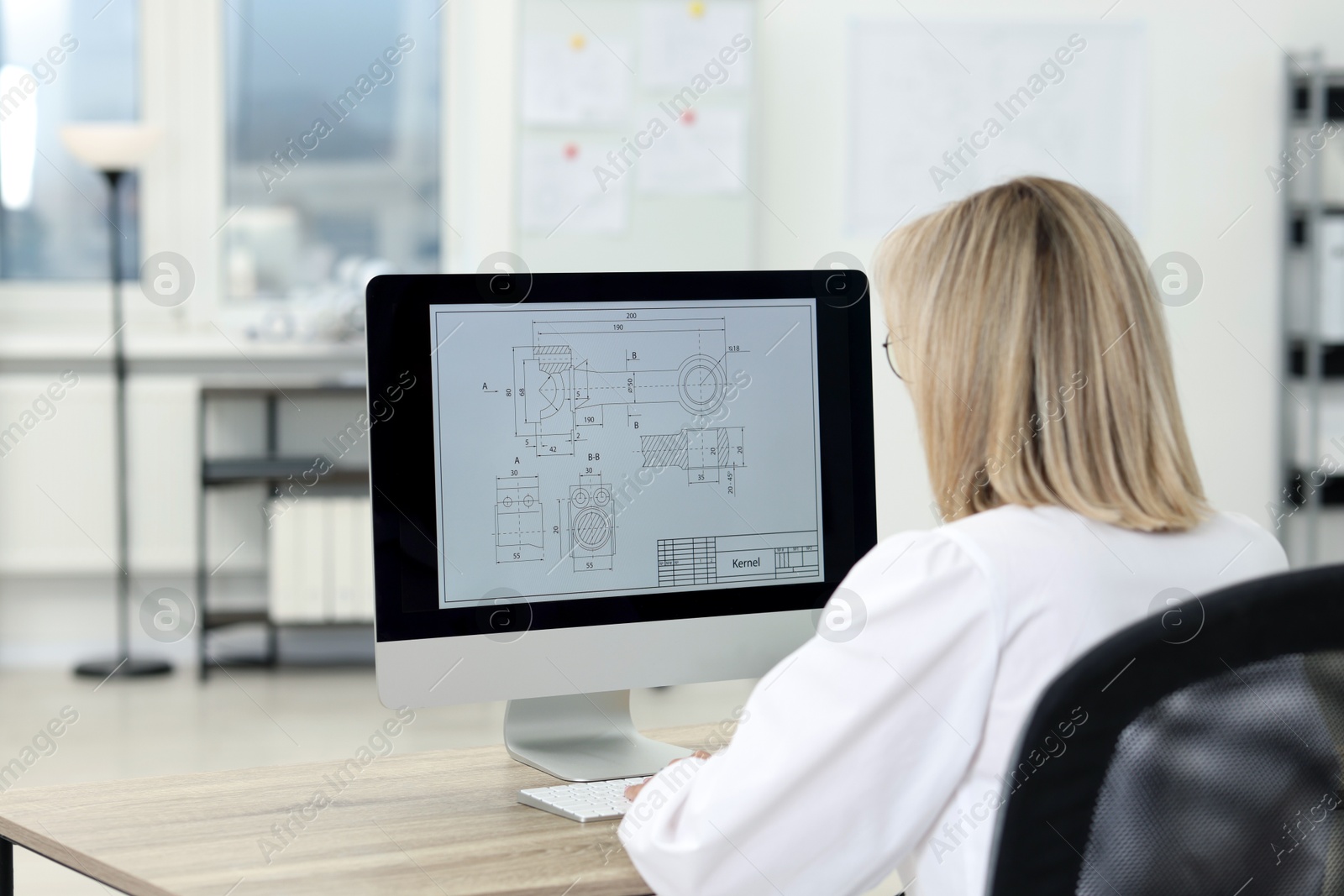 Photo of Technician making digital engineering drawing on computer at desk in office, back view