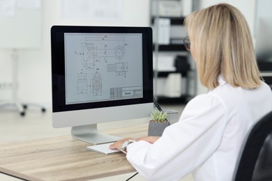 Photo of Technician making digital engineering drawing on computer at desk in office, back view