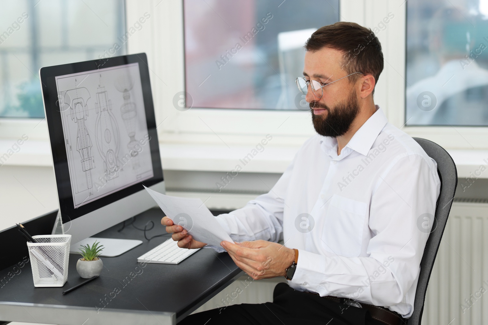 Photo of Technician making digital engineering drawing on computer at desk in office