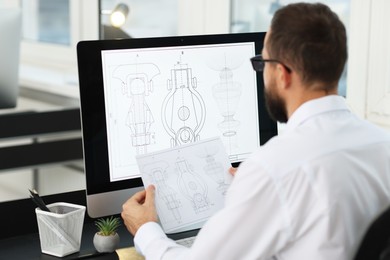 Photo of Technician making digital engineering drawing on computer at desk in office, back view