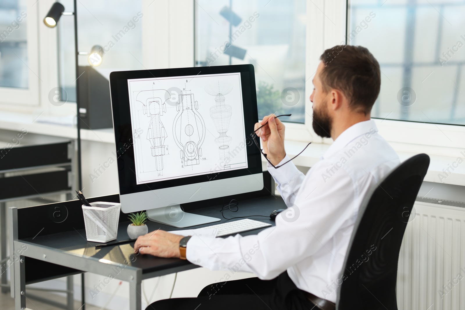 Photo of Technician making digital engineering drawing on computer at desk in office