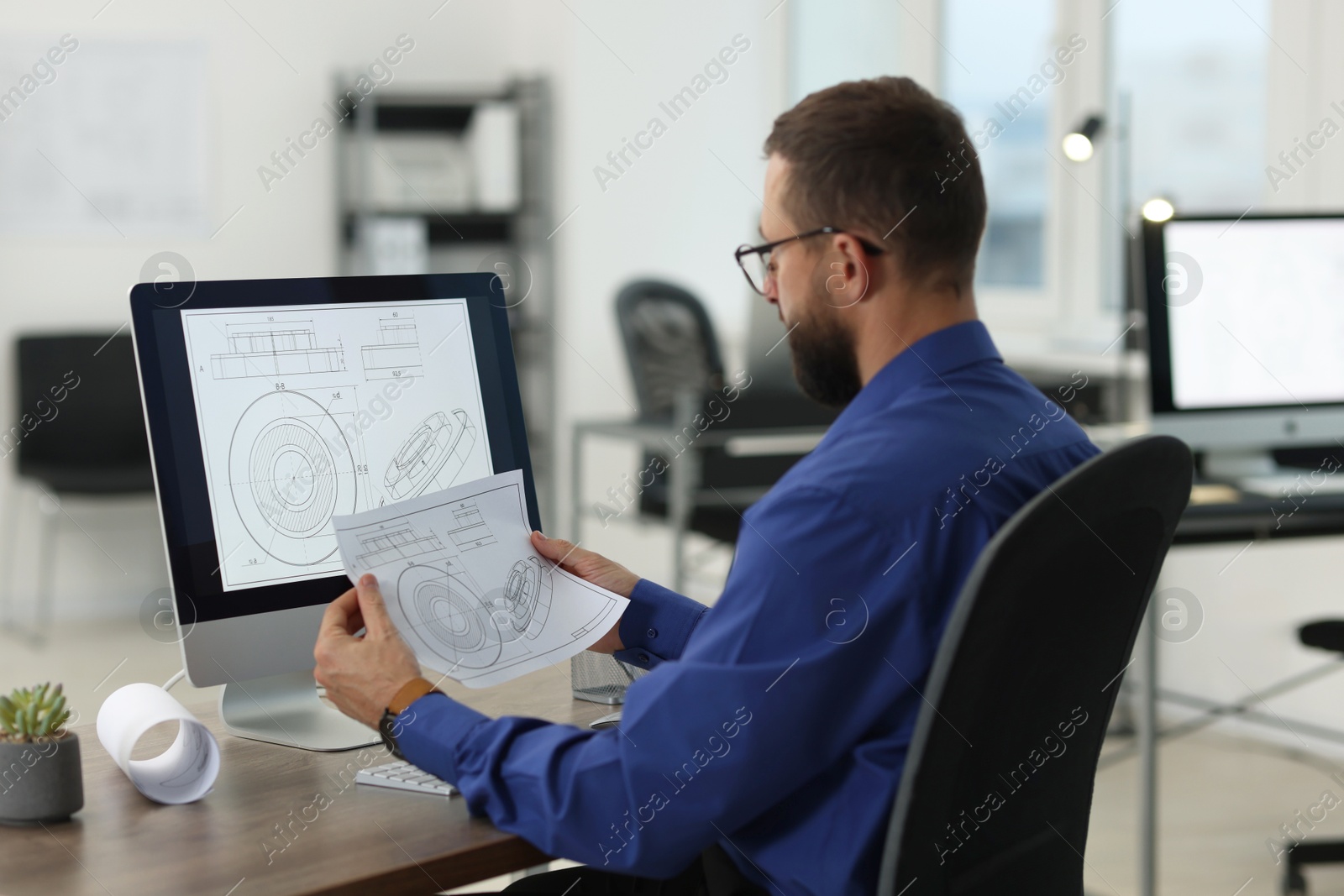 Photo of Technician making digital engineering drawing on computer at desk in office, back view