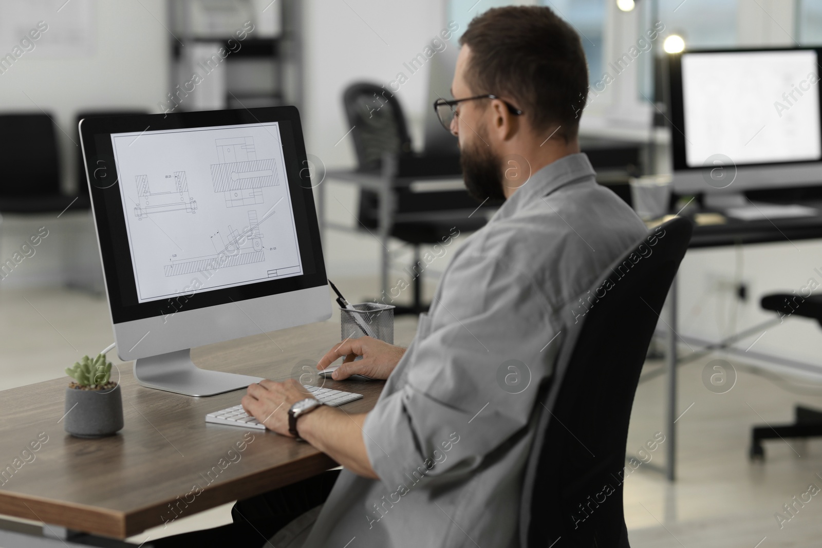 Photo of Technician making digital engineering drawing on computer at desk in office