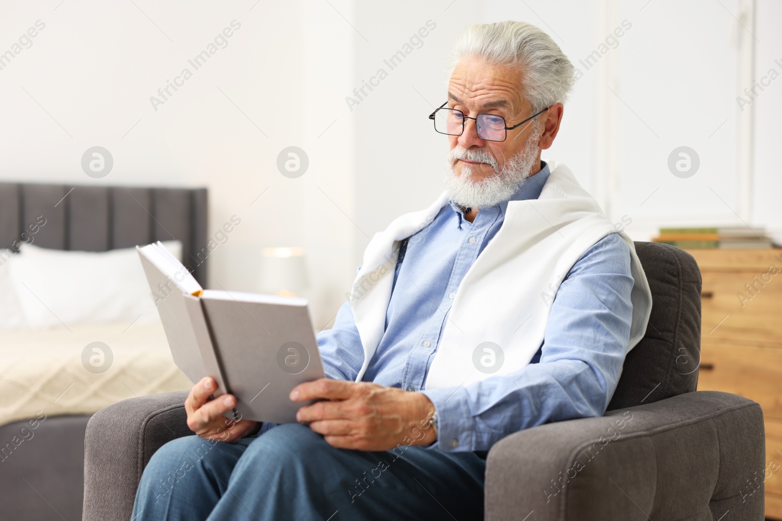 Photo of Handsome bearded man reading book in armchair at home