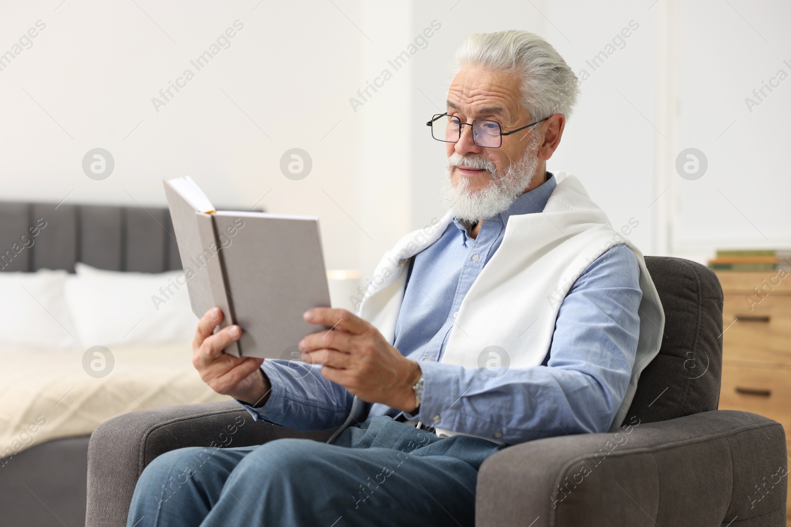 Photo of Handsome bearded man reading book in armchair at home