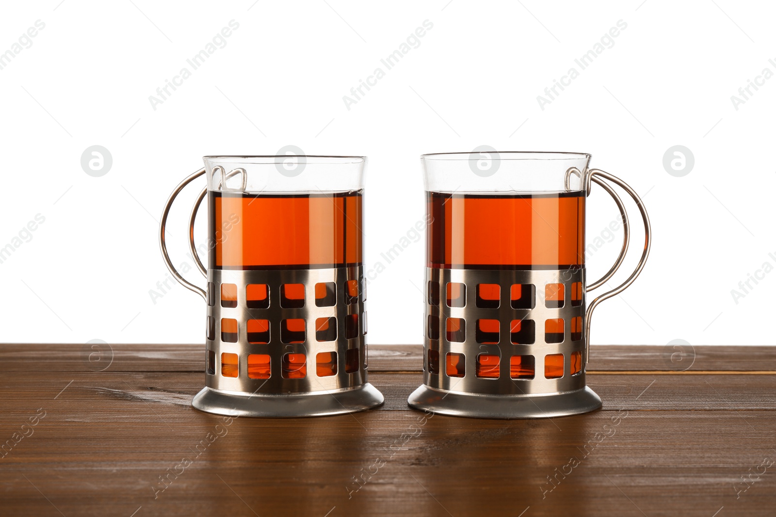 Photo of Glasses of aromatic tea in holders on wooden table against white background