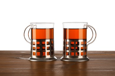 Glasses of aromatic tea in holders on wooden table against white background