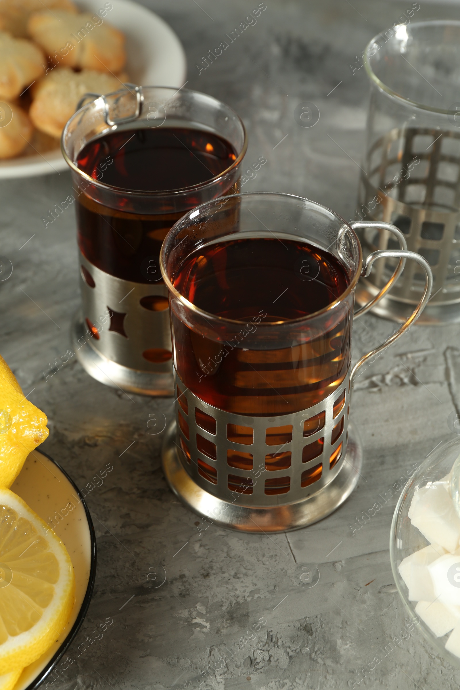 Photo of Glasses of tea in metal holders served on grey textured table, closeup