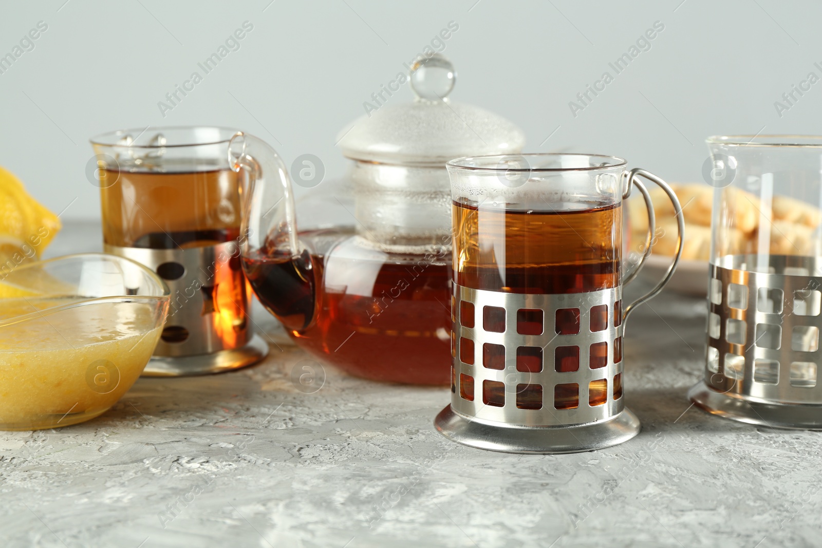 Photo of Glasses of tea in metal holders served on grey textured table, closeup