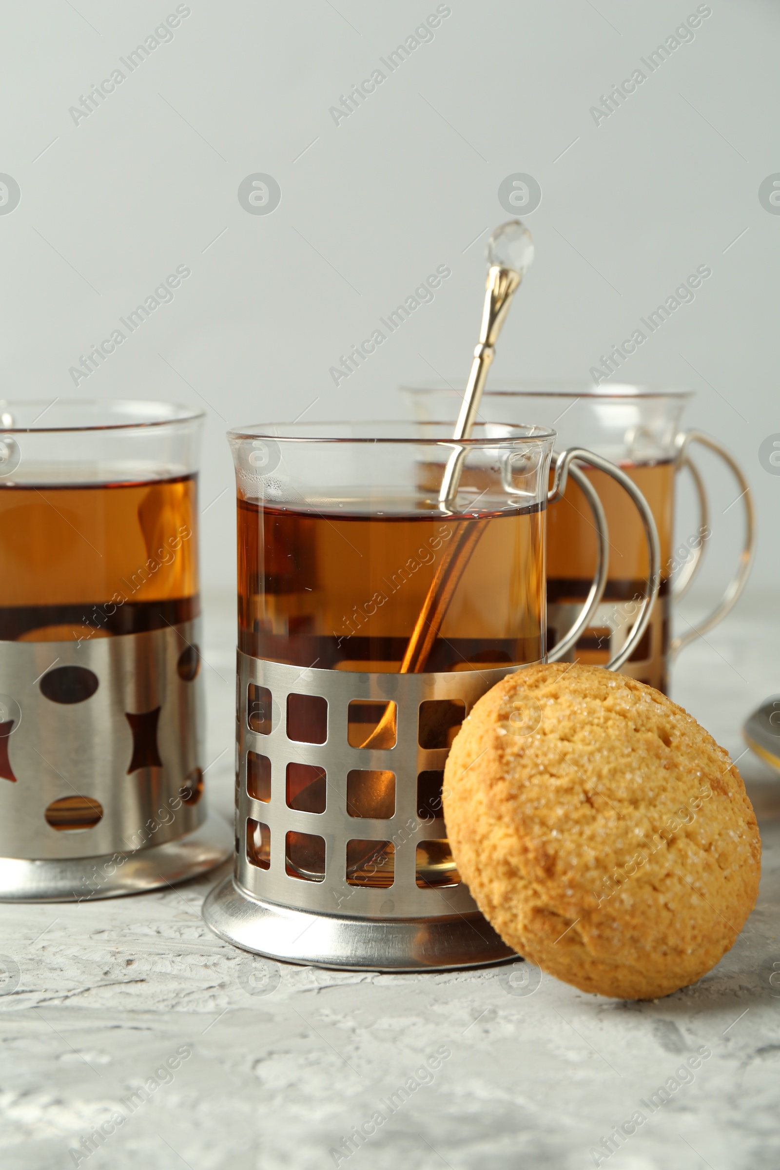 Photo of Glasses of tea in metal holders served on grey textured table, closeup