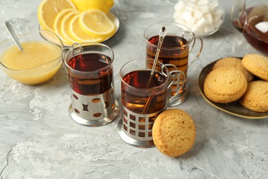 Photo of Glasses of tea in metal holders served on grey textured table