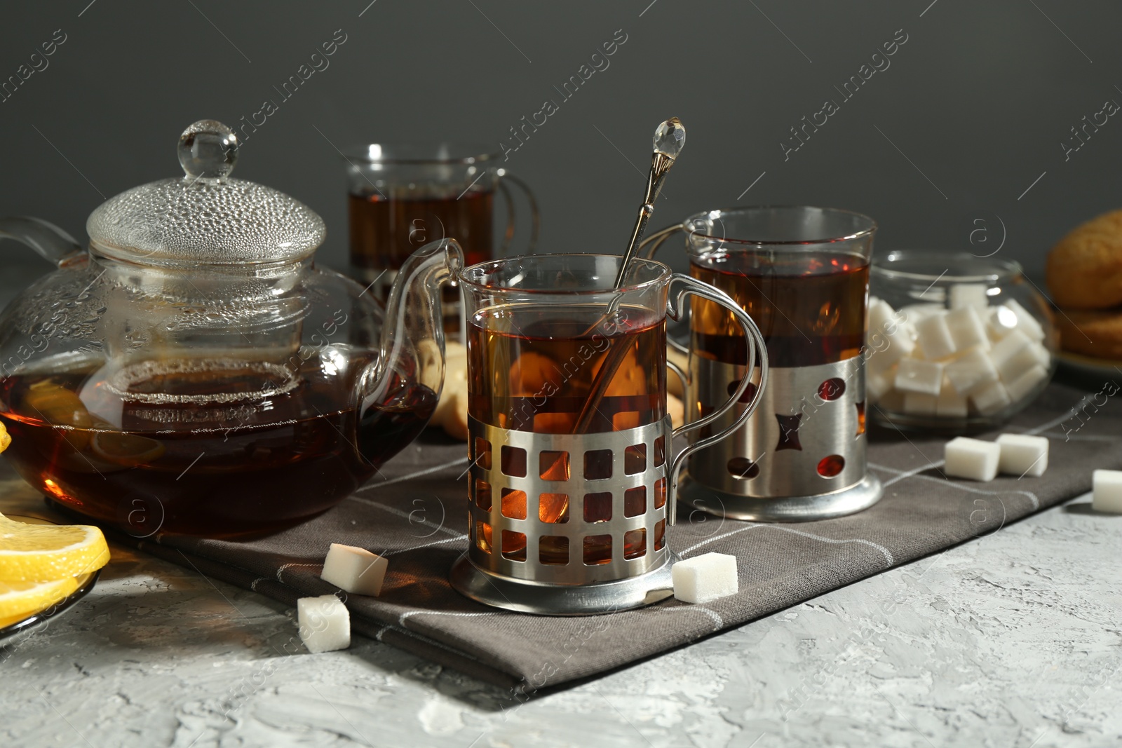 Photo of Glasses of tea in metal holders served on grey textured table