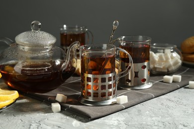 Photo of Glasses of tea in metal holders served on grey textured table